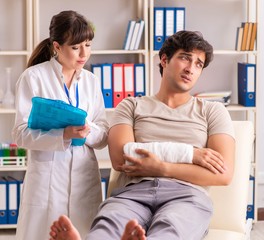 Young man with bandaged arm visiting female doctor traumatologis