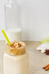 Iced Dalgona Coffee, a trendy fluffy creamy whipped coffee. Bottle of milk, spices on a light background. Glass mug close up. Vertical position.