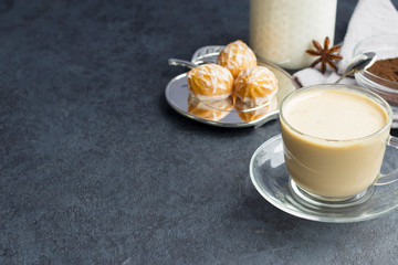Traditional indian black tea. Masala tea. Tea with spices and milk in a glass cup with a saucer and sweets on a dark background. horizontal position. Copy space.