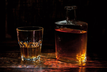 A glass of alcohol near a bottle. Old whiskey bottle on black wooden table. Drinks on a dark blurred background.