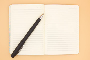 blank notebook with black pen on orange background, business planing concept. Space for text. Close up. Mock up