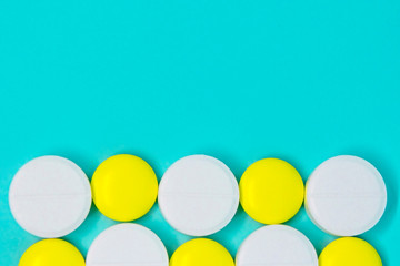white and yellow round pills in a row on a blue background close-up layout. medical treatment copy space concept 