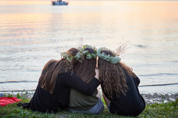 Three girls with wreaths of wild flowers by the lake. An evening at Saint John's Eve by the lake.