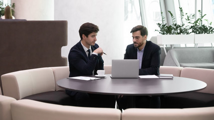 Partners sit at table in office lobby solve business issues together during meeting, mates prepare...