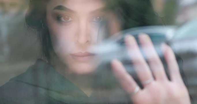 Sad woman with dark hair looking through window, grief and loneliness