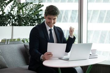 Businessman sit at desk read paper financial documents feels excited by sales increase, celebrate...