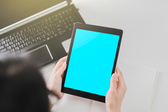 Technology concept: Woman holding a mock up of digital tablet device with Clipping path and notebook on white table in the background.