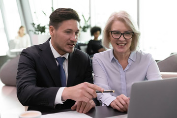 Different age colleagues sitting at desk inside of modern office hallway using computer discussing...