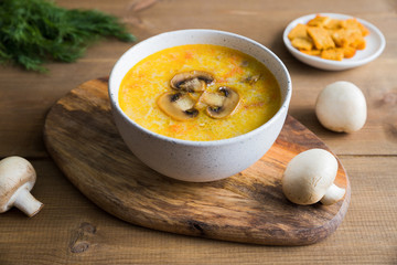Champignon soup in the white bowl with toast close up on the wooden stand. The whole mushrooms and a bunch of fresh green dill are lying next to on the table. The top of the soup is decorated mushroom