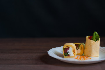 Sushi, vegetables, fish and cream cheese in egg pita on a white plate on dark background front view