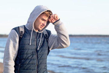young man suffering a headache on the background of the bay outdoors. Handsome guy holding his head on the background of the sea