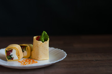 Sushi, vegetables, fish and cream cheese in egg pita on a white plate on dark background front view