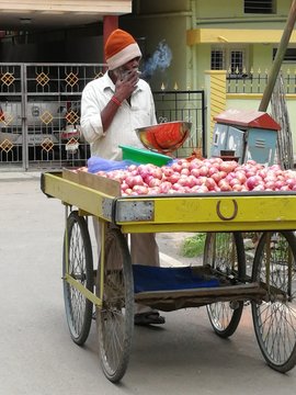 Male Vendor Smoking Cigarette While Selling Onions On Cart In City