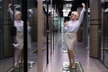 Elegant satisfied middle-aged businesslady company owner standing in office hallway dancing enjoy...