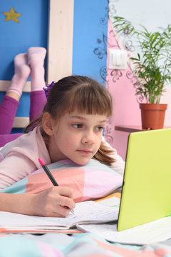 Schoolgirl watches video tutorials in a tablet computer and lies in bed