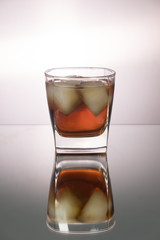 Glass of whiskey with pieces of ice on mirroring table. Vertical image with copy space.