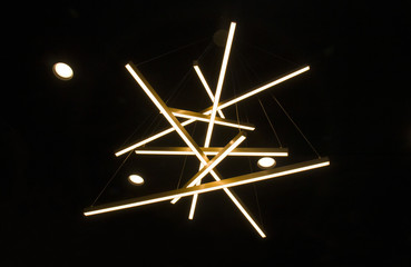 Original ceiling lamp in the form of long sticks, performing a decorative function of yellow on a black background