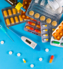 electronic thermometer, pills or vitamins on blue background