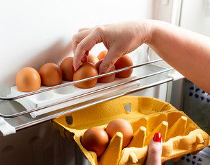 Manual collection of chicken eggs from cardboard packaging in the refrigerator. Organic Chicken Eggs Keep Fresh In The Fridge. Brown eggs in the tray. 