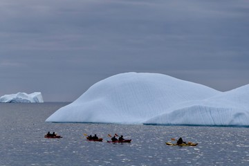 Kayaks in antarctic ocean before icebergs and dark clouds, Antarctica