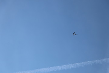 Small airplane and contrail on clear blue sky as background with copy space
