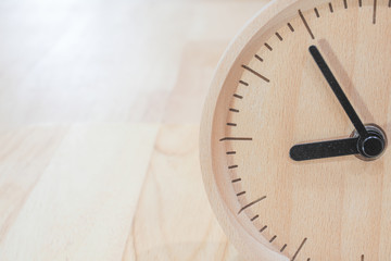 The close-up picture of the wooden table clock with a black dial showing about 9 o'clock on the wooden table as a background with warm light