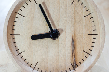 The close-up picture of the wooden table clock with a black dial showing about 9 o'clock on the wooden table as a background with warm light