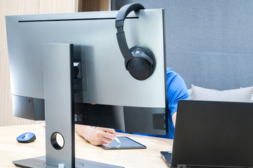 The man with a blue T-shirt is working with a black notebook behind the 27-inch monitor and there...