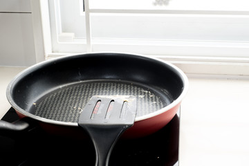 The unwashed pan and spatula put on the induction cooker with the sunlight from the window.