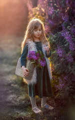 
girl with long hair in a basket standing in the sunset light in spring in the lilac bushes