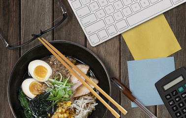 Top View of Working Space with Paper Notes, Ramen noodle, Computer, Pen, Eye Glasses and a...