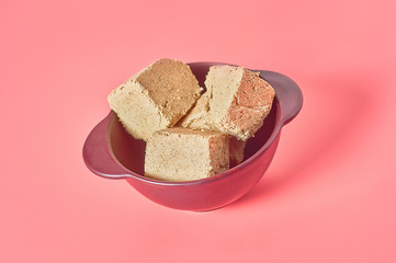 Pieces of sunflower halva lies in bowl on pink background. Turkish sweets