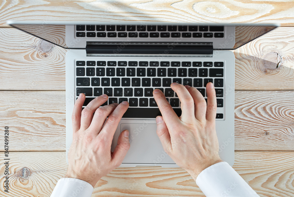 Aufkleber top view of man's hands typing on laptop in sunny day. coworking or working at home concept image.