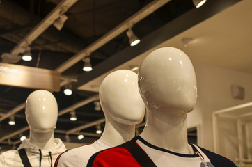 three white mannequin heads hairless and faceless in a clothing store spotlights shine on the ceiling