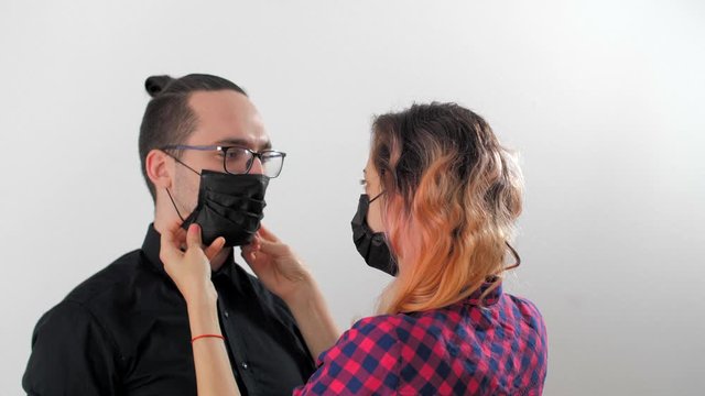 Portrait of modern family,  wife puts a medical mask on her husband. Attractive man and beautiful woman shows how to wear a medical mask. Virus prevention coronavirus or covid-19 concept.
