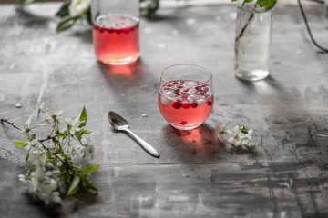 Spring cranberry lemonade in a glass on a gray shabby table with cherry flowers and leaves