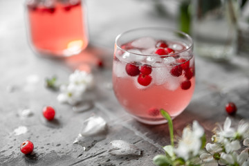 Spring cranberry lemonade in a glass on a gray shabby table with cherry flowers and leaves
