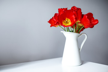 A beautiful bouquet of red tulips is standing in a white jug on the table. Festive bouquet as a gift. Focus on flowers. The concept of surprise.