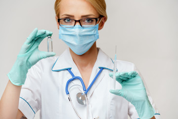 medical doctor nurse woman wearing protective mask and gloves - holding bottle of vaccine medicine and syringe