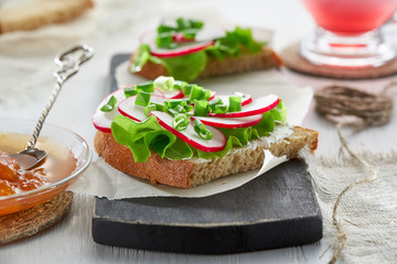 Sandwich with cottage cheese, radish, green onions and lettuce on a chopping Board.