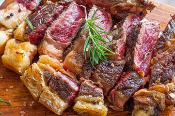 Freshly grilled juicy vaca rubia gallega steak cut in slices on a wooden board with rosemary, himalayan salt and pepper in grains