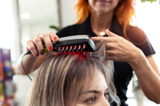 Hairdresser doing a treatment with ultrasonic and infrared laser comb for hair regrowth in her woman client at the salon.