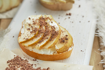 Sandwich with soft cheese, pieces of pear sprinkled with chocolate on a white wooden table.