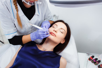 Young woman having permanent makeup on lips in beautician salon. Close up
