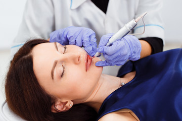 Young woman having permanent makeup on lips in beautician salon. Close up