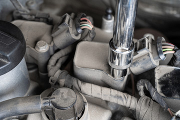 Socket wrench loosening screw on ignition coil in car engine bay. Mechanic repair or vehicle...