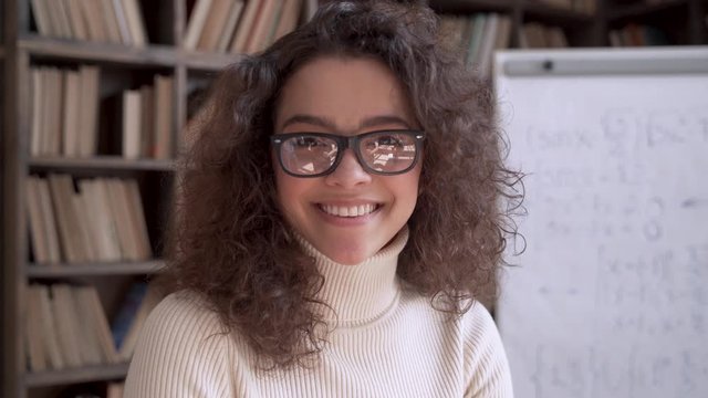 Smiling confident latin lady ethnic young woman university teacher, happy hispanic woman student, professional tutor wear glasses looking at camera laughing standing in classroom. Close up portrait.