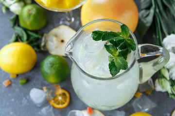 Summer fresh cold drink beverages. Ice Lemonade in the jug and lemons and orange with mint on the table outdoor. Orange lemonade in a jug
