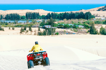 Tourist enjoy riding the quad bike or powerful fast off-road four-wheel drive ATVs at white sand dunes in Mui Ne, Vietnam.