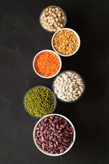 Obraz na płótnie Canvas Various sources of vegetable protein: beans, lentils, peas, chickpeas, mung bean in bowls. A healthy balanced diet for vegans and vegetarians. Dark background. Top view, vertical orientation.